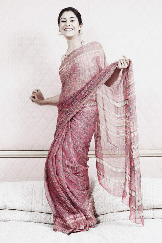 一个人,站,举,笑,微笑,露齿笑,竖图,室内,白天,正面,民族服装,床,卧室,亚洲,仅一个年轻女性,仅一个女性,仅一个人,墙,双人床,床单,注视,被子,墙壁,墙面,扶,观察,看,托,站着,服饰,观看,飘逸,察看,被单,扶着,庄重,关注,追求,纱丽,雅致,纱丽服,清婉,妍丽,年轻女性,女人,女性,亚洲人,印度人,举起,举手,举着,向上举,向上伸,向上托,站立,彩图,全身,传统服装,民俗服,睡房,卧房,奢华