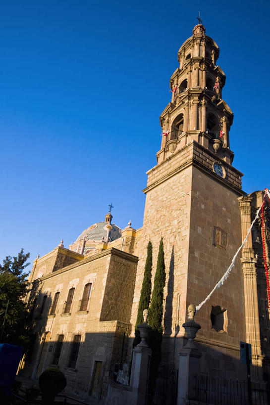 无人,教堂,竖图,室外,白天,仰视,旅游,度假,植物,标志建筑,地标,建筑,墨西哥,阴影,节日,时间,光线,时钟,影子,墙,钟楼,计时,文化,娱乐,建设,墙壁,墙面,树,树木,蓝色,绿色,蓝天,天空,阳光,自然,钟表,天,祈祷,享受,休闲,健康,表,旅游胜地,放松,许愿,宗教,信仰,生长,晴朗,成长,纪念,祈求,北美,北美洲,基督教,天主教,美洲,信念,万里无云,阿瓜斯卡连特斯州,阿瓜斯卡连特斯,北亚美利加洲,亚美利加洲,塔钟,墨西哥合众国,仙人掌王国,平安,钟,晴空,晴空万里,彩图,低角度拍摄,大教堂,礼拜堂