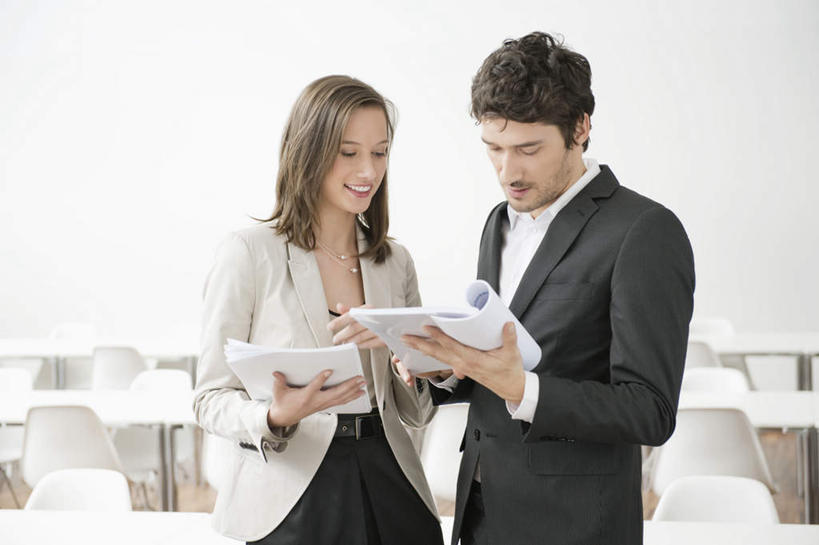 西方人,两个人,伙伴,朋友,商务人士,商务男性,商务女性,站,捧,笑,微笑,露齿笑,横图,室内,白天,正面,衬衫,友谊,合作,团队,桌子,书籍,椅子,欧洲,欧洲人,套装,塑料,办公桌,墙,注视,墙壁,墙面,白色,塑料制品,观察,看,站着,战略,观看,察看,关注,商务装,工薪阶层,联合,合谋,配合,协作,男人,男性,年轻男性,年轻女性,女人,女性,白种人,白领,上班族,书,图书,端,端着,捧着,手捧,站立,半身,彩图,衬衣